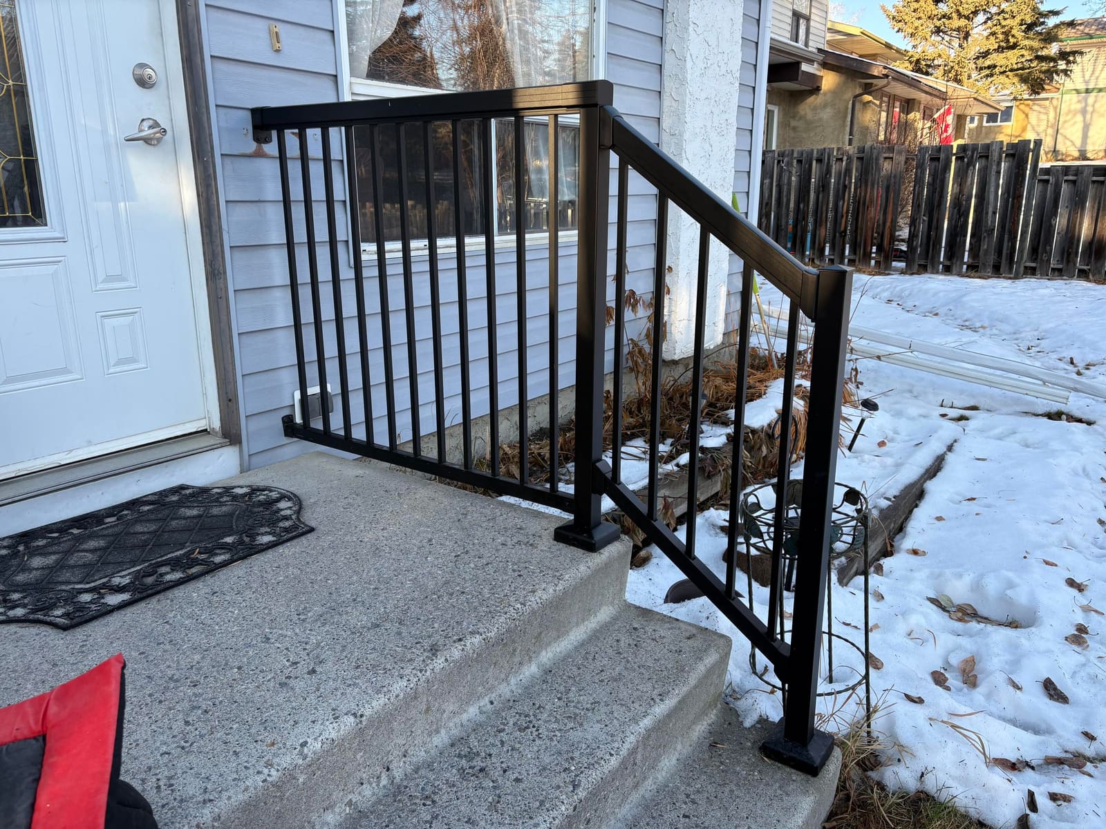 A black powder-coated aluminum handrail and guard installed at the front step of a home