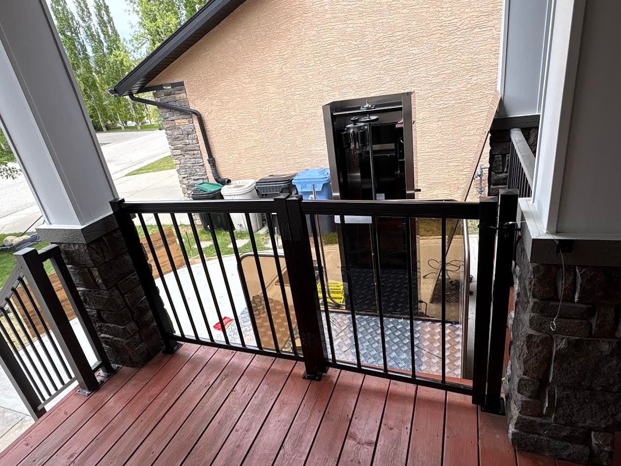 A vertical platform lift installed beside a raised rear deck, with an aluminum safety gate at the top landing